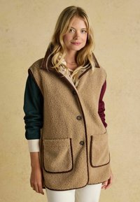 Beige Fleeceweste mit braunem Kragen, zwei Fronttaschen und brauner Einfassung. Das Design verfügt über Knöpfe entlang der Vorderseite und lange Ärmel darunter.