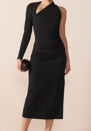 Vestido negro ceñido con diseño asimétrico, una manga larga y un ajuste drapeado. Tejido suave y corte a la altura de la rodilla. Combinado con un accesorio oscuro.