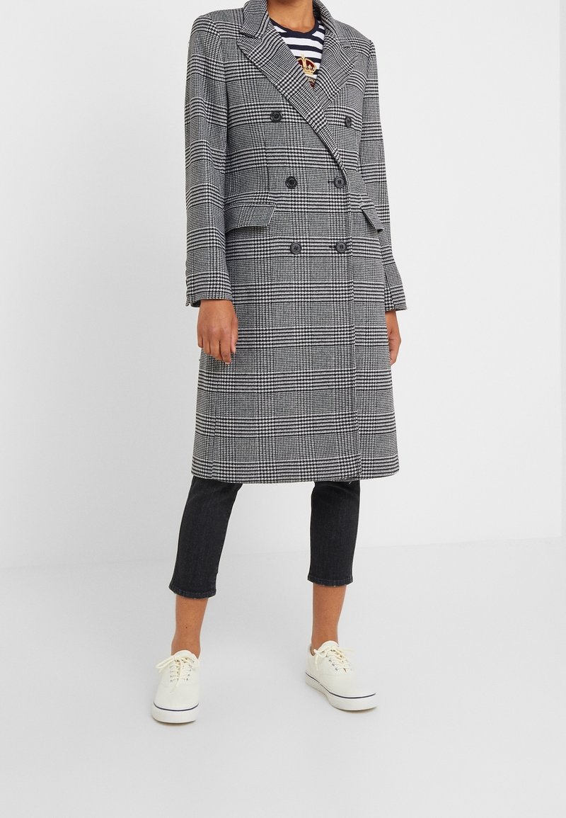 Černobílý kabát s houndstooth vzorem, dvouřadový, s velkými klopami, předními kapsami a přímým střihem. V kombinaci s tmavými džíny a bílými teniskami.