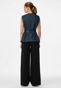 Top de mezclilla sin mangas con rayas blancas verticales, ceñido en la cintura con un cinturón, combinado con pantalones anchos negros. Líneas limpias y ajuste estructurado.