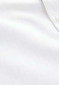 Witte shirtstof met een subtiel geometrisch patroon, een gladde textuur en knoopdetails bij de kraag.