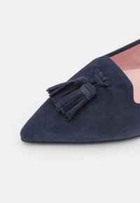 Bottines plates en suede bleu marine avec un bout pointu, ornées d'un accent de glands décoratif et d'une doublure intérieure rose contrastante.