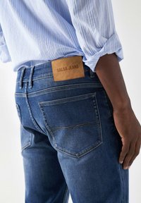 Tamno plave traperice s kožnom oznakom Salsa Jeans na pojasu. Klasični dizajn s pet džepova i detaljna šavova na stražnjim džepovima.