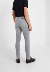 Světle šedé skinny džíny vyrobené z denimu, s středně vysokým pasem a dvěma zadními kapsami. V kombinaci s černým tričkem a černými teniskami.