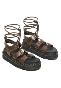 Sandali platform in pelle marrone con cinghie incrociate, suola nera piatta, lacci marroni e cuciture gialle lungo il bordo della suola.