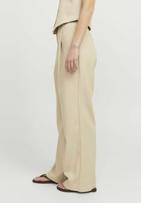 Beige wijde broek gemaakt van lichte stof, met een hoge taille en plooien, gecombineerd met platte sandalen. Eenvoudige en gladde textuur.