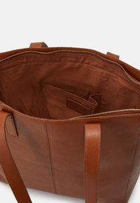 Bruine leren tote bag met een ritssluiting, een open interieur en een klein binnenvak. Gestructureerde afwerking en platte handvatten.