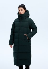 Lang, mørkegrøn pufferjakke med stor hætte, lodret quiltet design, lynlås lukning og sidelommer. Blødt, isoleret materiale.
