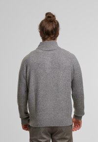 Gray wool sweater with a high ribbed collar, dropped shoulders, and ribbed cuffs and hem. Soft texture and relaxed fit.