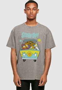 Camiseta gris de gran tamaño que presenta un diseño de una furgoneta colorida con personajes de Scooby-Doo, decorada con flores y elementos de dibujos animados.