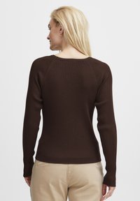 Maglione marrone a coste con maniche lunghe, scollo tondo e design aderente, caratterizzato da tessuto testurizzato e maniche raglan.
