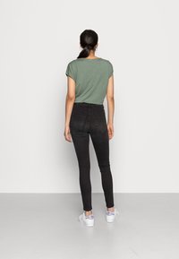 Grön kortärmad topp kombinerad med högmidjade svarta jeans och vita sneakers. Tyget verkar mjukt och jeansen har bakfickor.