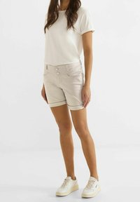 Ljusbeige denimshorts med uppvikta fållar, två framfickor och knappstängning. Stylingen kompletteras med en enkel vit t-shirt och vita sneakers.