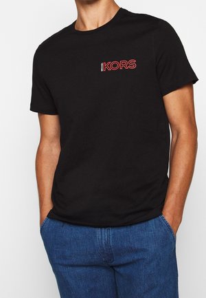 T-shirt en coton noir avec col rond, arborant un petit logo rouge "MICHAEL KORS" sur la poitrine gauche. Manches courtes et coupe régulière.