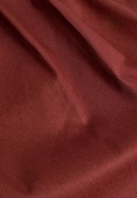 Tissu bordeaux avec une texture lisse, présentant des plis subtils et une finition légèrement brillante. Le matériau semble léger et flexible.