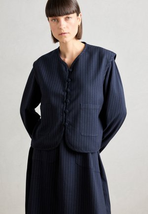 Marineblå pinstripe vest med rund hals, knaplukning og påsatte lommer. Har et strømlinet design og glat stoftekstur.
