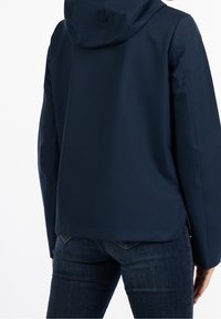 Chaqueta con capucha de color azul marino, con una textura suave y mate, que presenta un corte recto y aberturas laterales, combinada con pantalones de mezclilla oscuros.