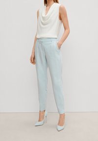 Pantalon bleu clair ajusté avec une texture lisse, associé à un haut blanc sans manches avec un col drapé. Chaussures à talons hauts.