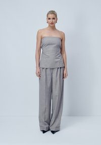 Top grigio senza spalline con un design aderente, abbinato a pantaloni grigi a gamba larga; texture liscia e leggera lucentezza; tacchi neri a punta.