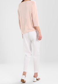 Top in magenta chiaro, morbido e dal taglio ampio con maniche a tre quarti, abbinato a pantaloni bianchi. Modella che indossa sandali bianchi con tacco a blocco.