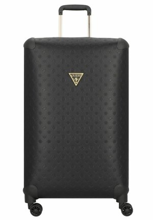 Valise rigide noire en matériau texturé, arborant un logo triangulaire doré. Équipée d'une poignée télescopique et de quatre roues.