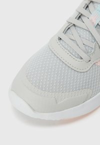 Chaussure de sport gris clair avec une tige en maille respirante, des accents synthétiques lisses et une semelle en caoutchouc texturé. Présente des lacets plats et un détail minimal.