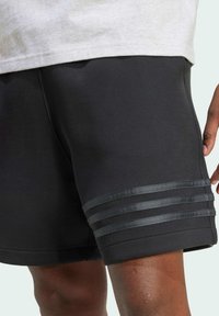Černé sportovní šortky vyrobené z měkké tkaniny, s hladkým povrchem a třemi vodorovnými pruhy v tmavší barvě na lemu.