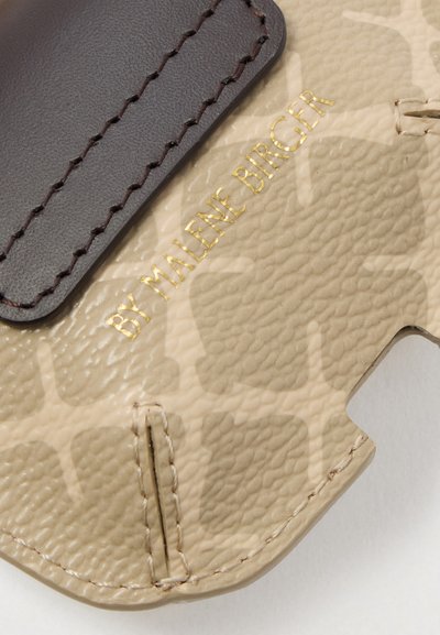 Prim-plan al unei piei texturate bej cu o curea din piele maro închis cusută și textul aurit embosat "BY MALENE BIRGER".