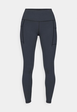 Leggings gris foncé en tissu extensible, avec une taille haute et deux poches latérales avec des surpiqûres noires contrastantes.