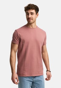 Camiseta de manga corta rosa con cuello redondo, hecha de un suave tejido de algodón. Presenta un corte relajado y detalles de costura sutiles.