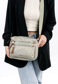 Světlé šedé crossbody taška vyrobená z měkké tkaniny s několika zipovými kapsami, hnědými koženými akcenty a dlouhým nastavitelným popruhem.