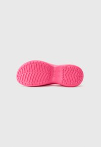 Semelle de chaussure en caoutchouc rose avec une prise texturée et à motifs. Forme arrondie, bords lisses et impression de marque visible sur la surface.