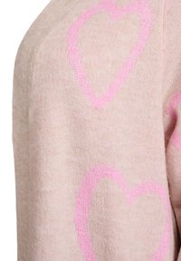 Gaiši rozā džemperis ar mīkstu tekstūru un lielām rozā sirdīm. Dizaina akcenti ietver noapaļotus plecus un ribota veida aproces.