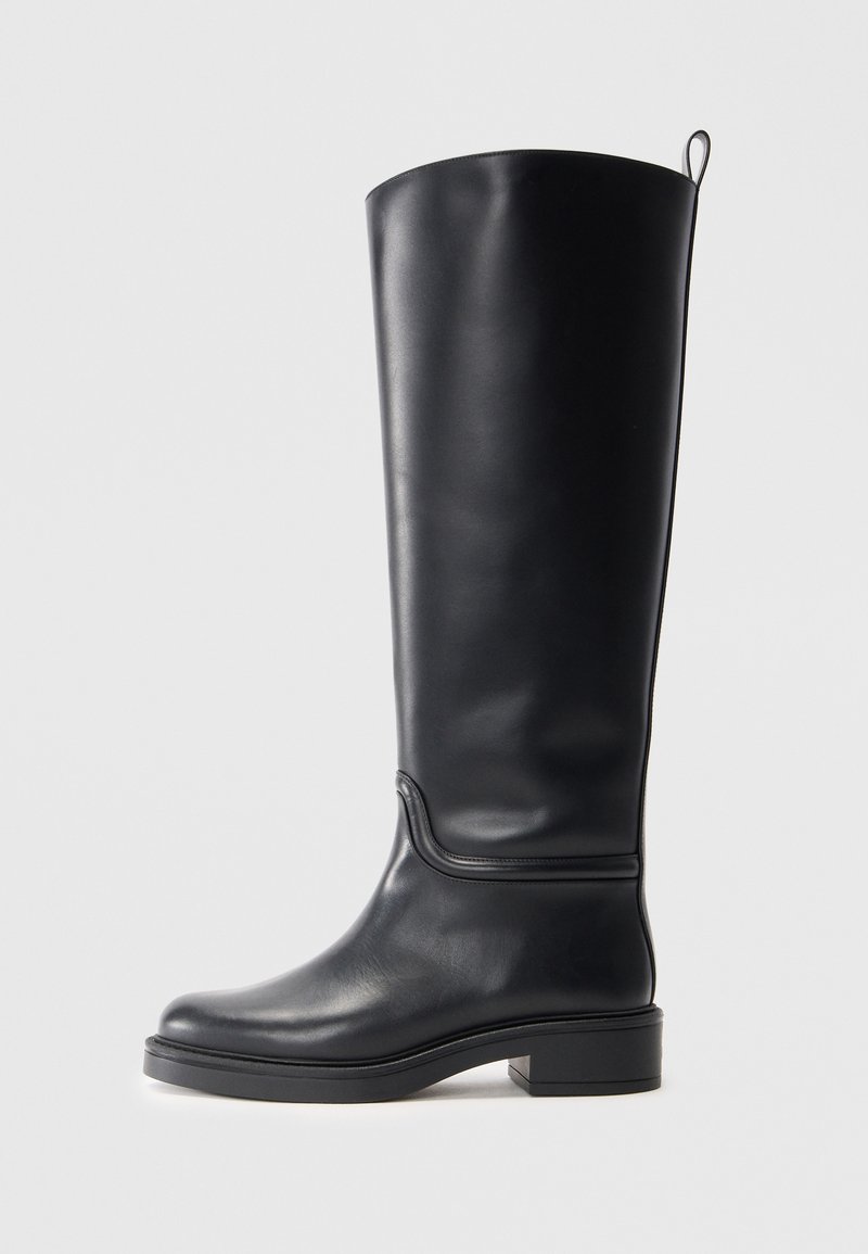 Botte en cuir noir hauteur genou avec une texture lisse, bout arrondi et semelle épaisse. Présente un détail de couture subtil et une languette en haut.