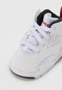 Hvit sneakers med teksturert syntetisk overdel, grå detaljer og rødt merke. Har hvite snørebånd, perforeringer og en svart gummisåle.