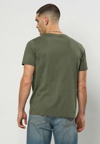 Olivengrønn t-skjorte laget av myk bomull, kortermet, normal passform og rund hals, kombinert med lyseblå denim jeans.