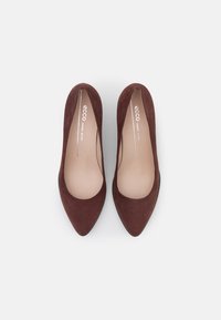 Décolleté con tacco alto in suede marrone, punta appuntita e finitura liscia, caratterizzate da un design minimalista e una soletta imbottita.