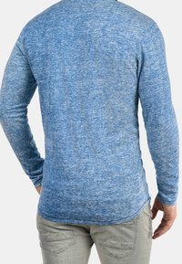 Chemise à manches longues bleue texturée avec un effet chiné, col rond et coupe slim, accompagnée d'un pantalon gris clair.