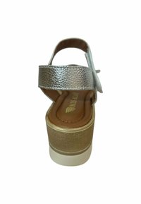 Sandalia de plata texturizada con una correa ancha, plantilla marrón y una suela de plataforma alta con un diseño acanalado. Vista trasera que muestra la altura del tacón.