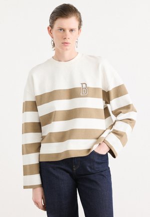 Striped sweater in beige and cream, featuring a round neck, long sleeves, and embroidered letter 'B' detail. Material appears soft and textured.