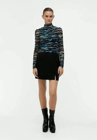 Camicia a maniche lunghe in tessuto trasparente a fantasia multicolore con colletto alto, abbinata a una mini gonna nera con fessure laterali. Stivali con plateau neri.