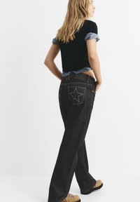 Jeans neri a gamba larga con ricami a forma di stella sulle tasche posteriori, abbinati a una maglietta cropped a righe nera e blu con maniche arrotolate.