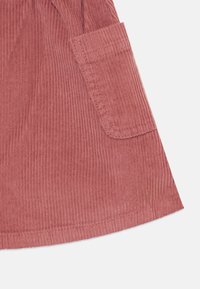 Kordfløyelstoff i rosa nyanse med vertikale ribbing. Rundet kant med en lommepatch på siden, pent synlig søm.