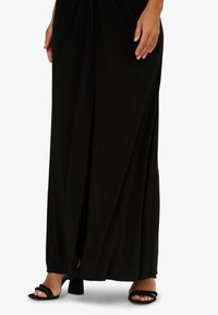 Černé maxi šaty s volným střihem, s rozparkem na jedné straně. V kombinaci s černými sandály na podpatku se sponami. Hladká textura látky.