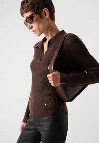 Rjav rebrast polo pulover z V-izrezom, okrašen s drobnimi bleščicami, v paru s črnimi usnjenimi hlačami in rjavim torbico čez ramena.