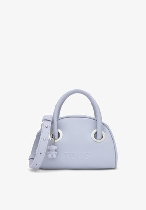 Jasnofioletowa skórzana torebka z zaokrąglonymi uchwytami, srebrnymi pierścieniami, regulowanym paskiem, tłoczonym logo "TOUS" oraz małą zawieszką w kształcie misia.