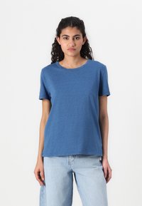 Blå kortermet t-skjorte laget av myk stoff, med rund hals og avslappet passform. Kombinert med lyseblå denimjeans.
