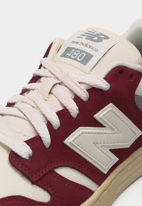 Κοντινό πλάνο σε αθλητικό παπούτσι New Balance 480 σε εκρού και μπορντό χρώμα με λευκά κορδόνια και μεγάλο λογότυπο N στο πλάι.