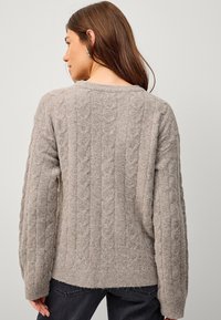 Jasnoszary sweter w splot rodzimy z teksturowanym wzorem, luźnym krojem i ściągaczem. Materiał wydaje się miękki i przytulny.