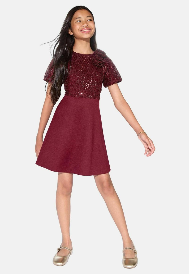 Burgundia kleit, millel on sädelev ülemine osa ja puhv-sleeved, sile seelik ja lilleline aksent. Kandmiseks kuldseid jalanõusid, millel on pehme sära.